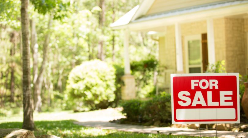 a house surrounded by trees with a for sale sign in front